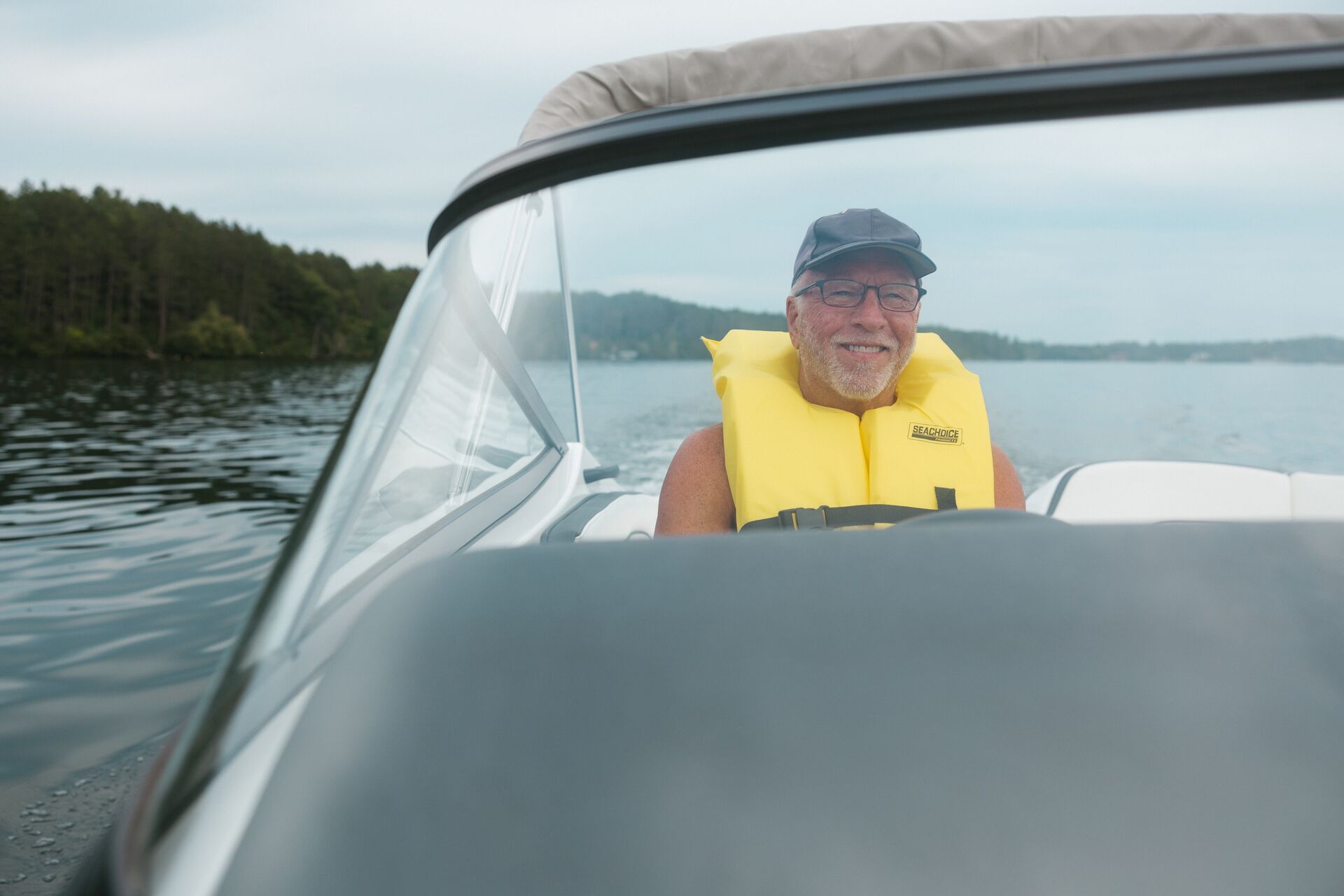 Man in a yellow life vest drives a boat, Minnesota boating regulations concept.