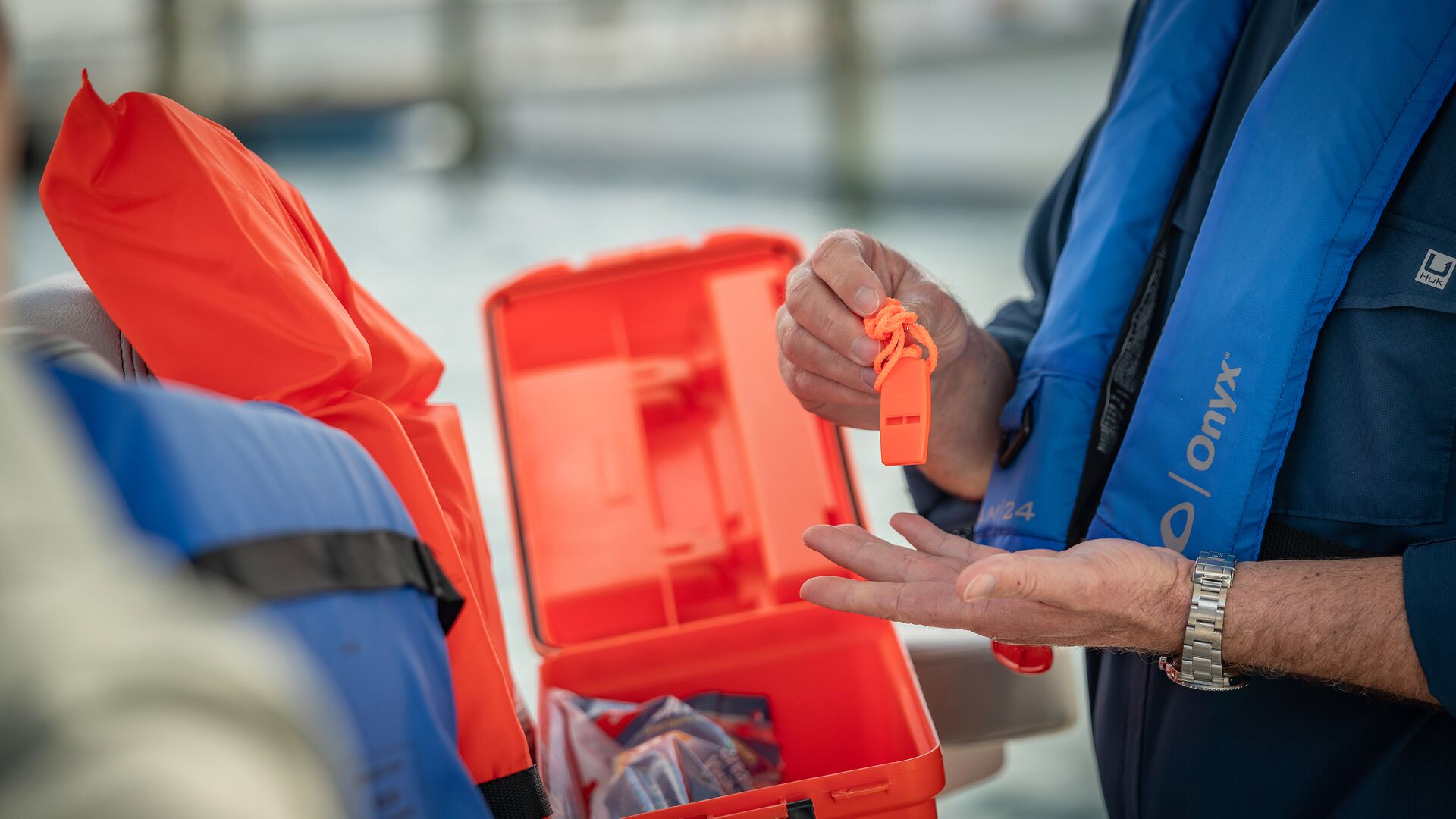 Man holds whistle from emergency kit on a boat, how to survive a shipwreck concept. 