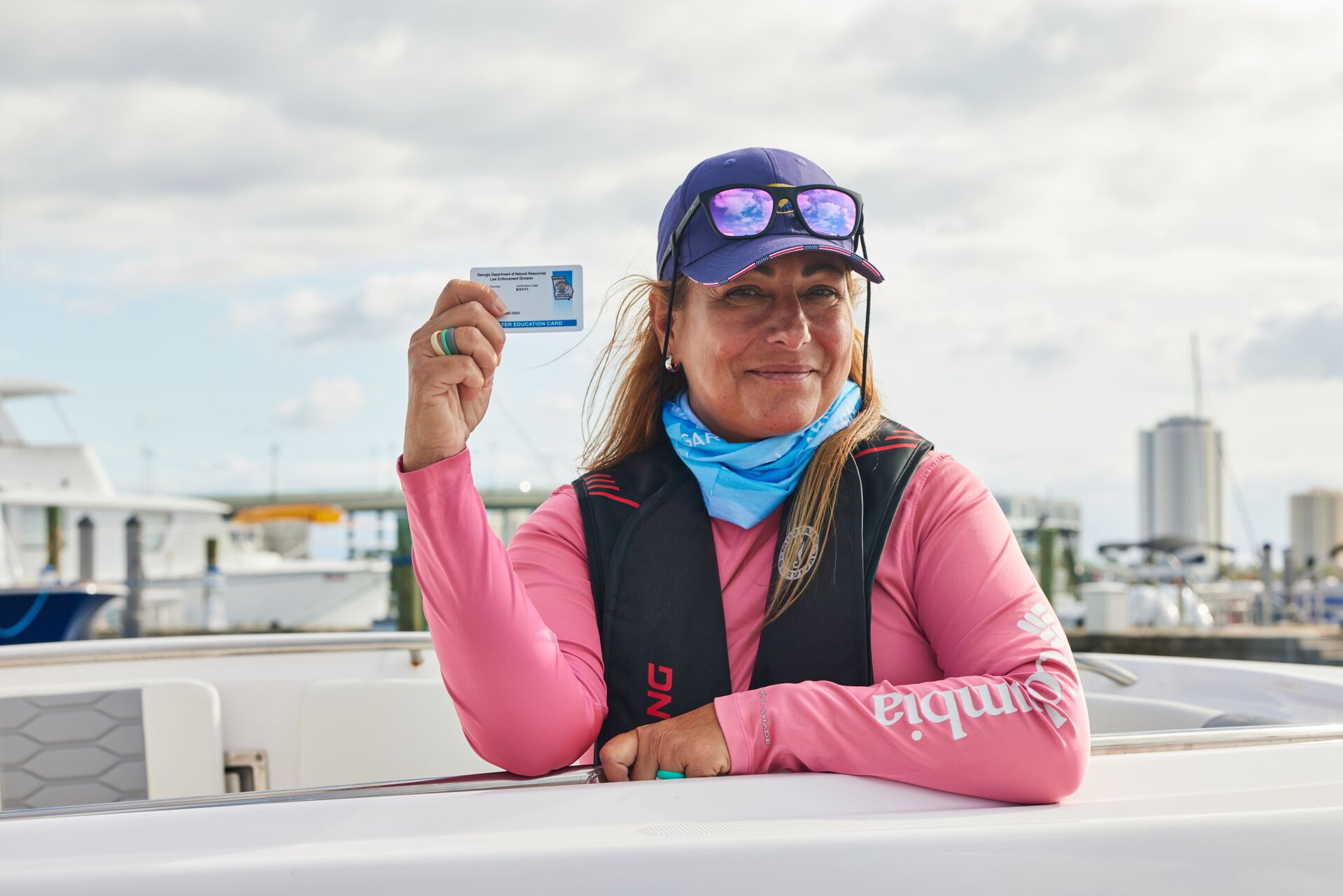 Woman wears life jacket holding boater education card.