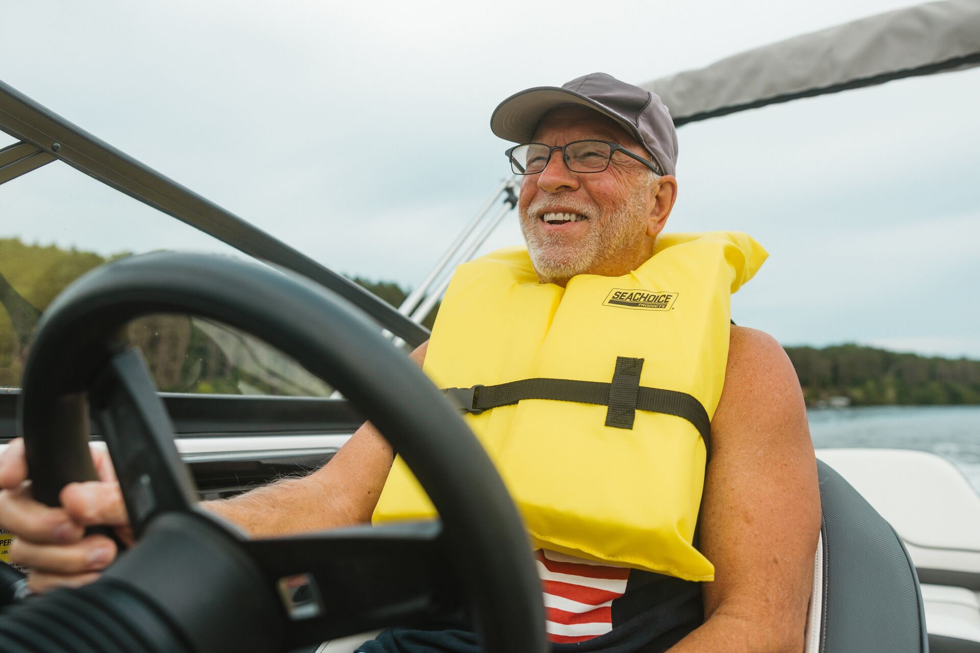 Man smiles, wears yellow life vest, drives boat, boating on the Hudson concept. 