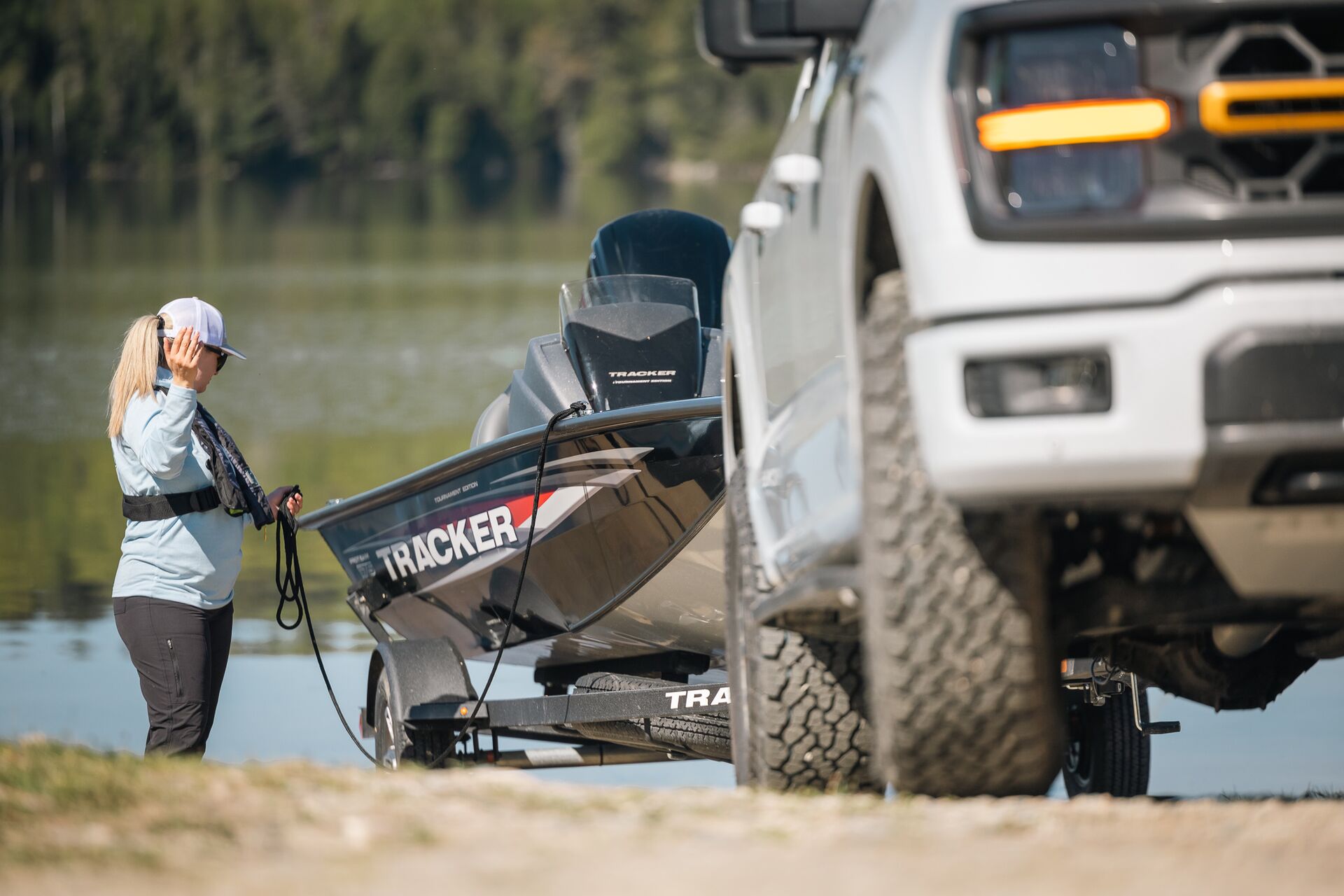 Woman directs directs truck backing trailer and boat into water. 