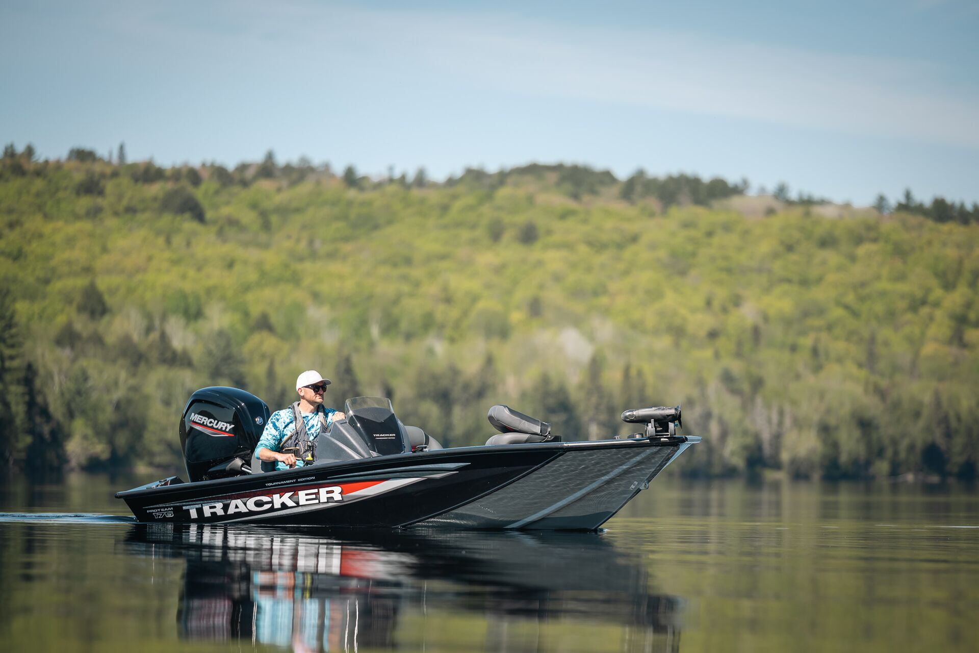 Man drives black fishing boat on calm water. 