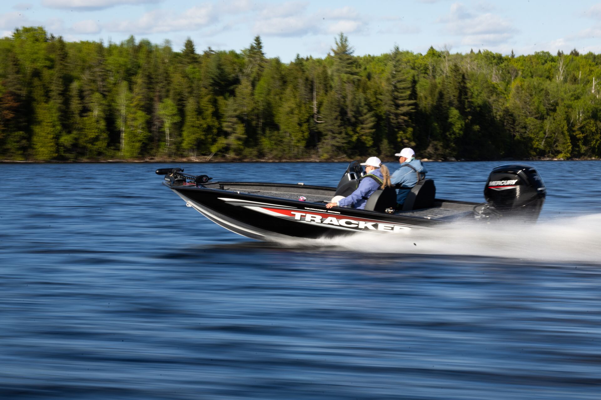 Two people in fast-moving black fishing boat. 