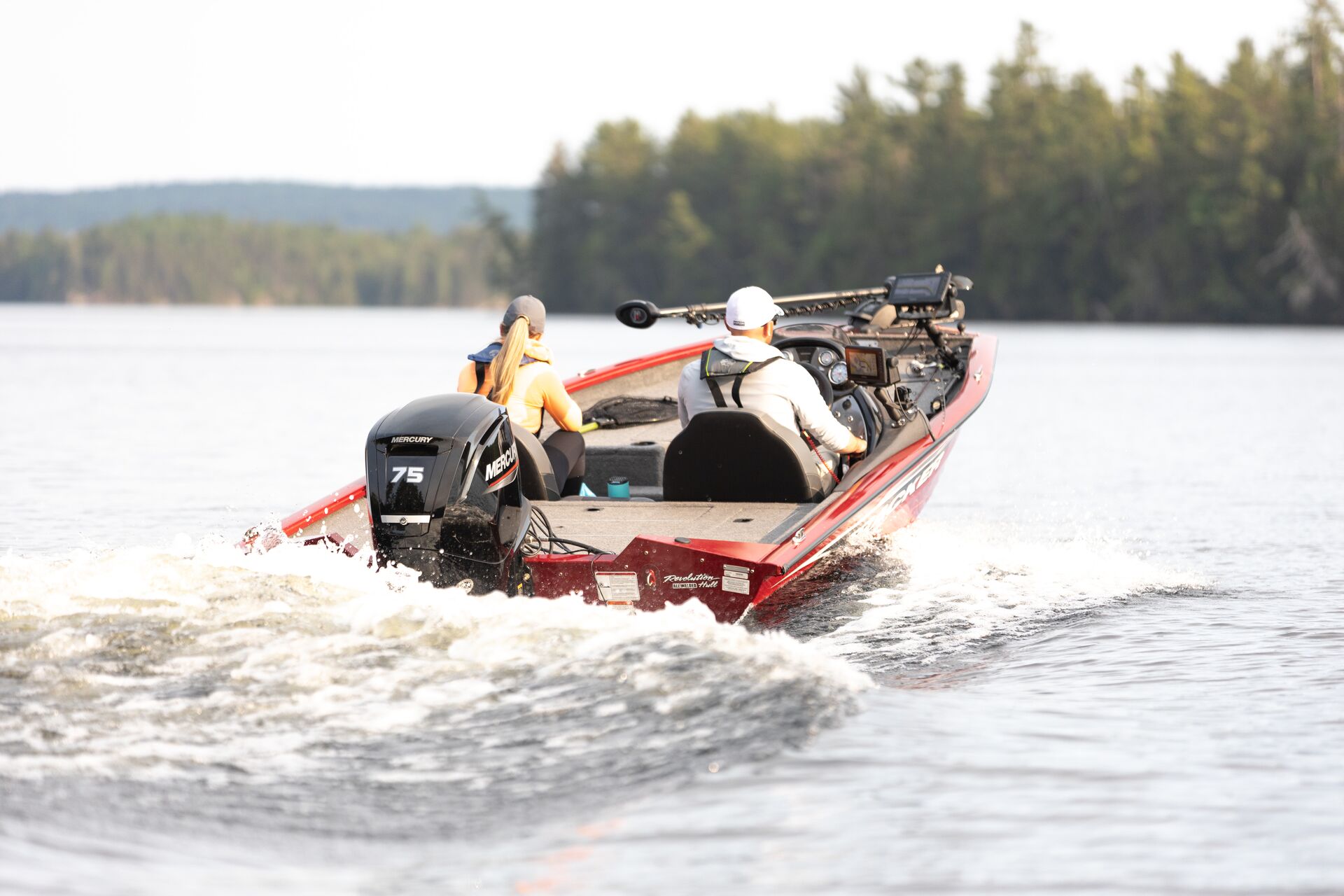 Two people drive away on the water in red bass boat.