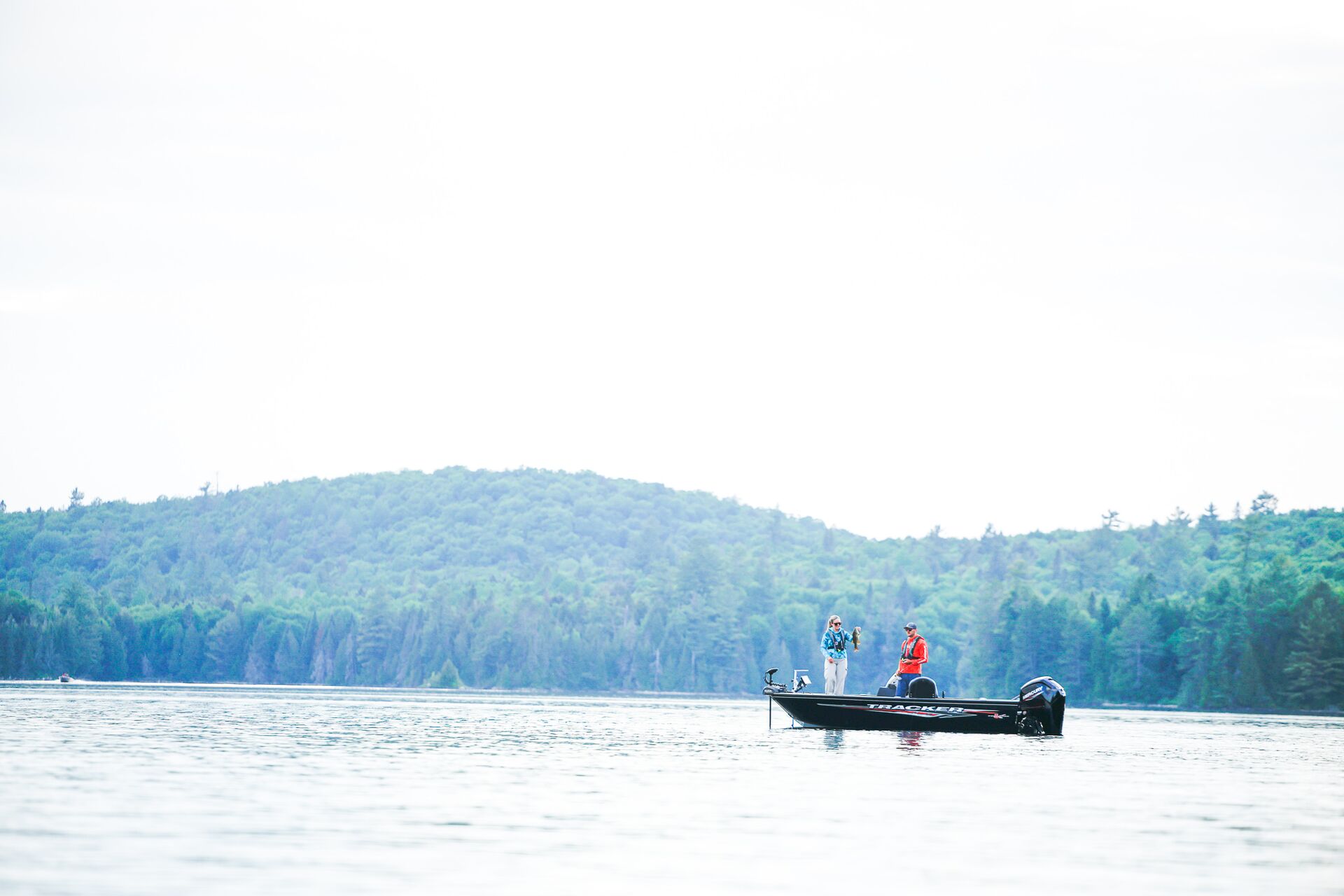 Two people on fishing boat in the distance on lake, BC boating license test concept. 