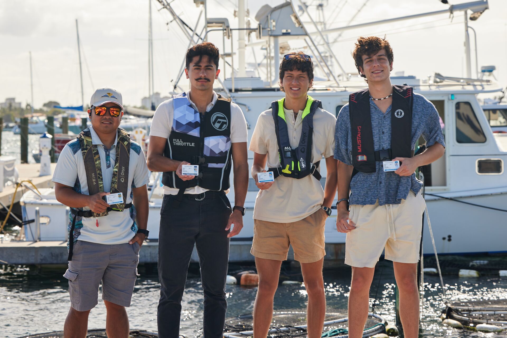 Four men wear life jackets while on dock holding boater cards, get Ontario boating license concept.