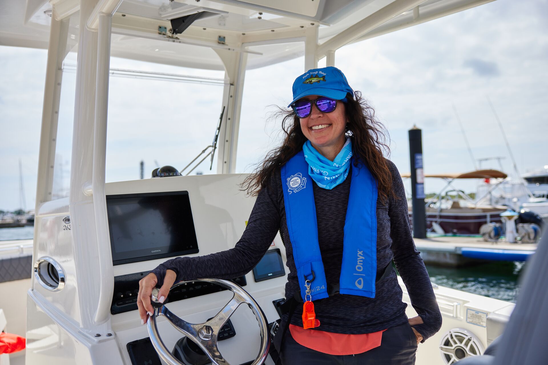 Smiling woman in blue life vest at helm of boat, boating certification Canada concept. 