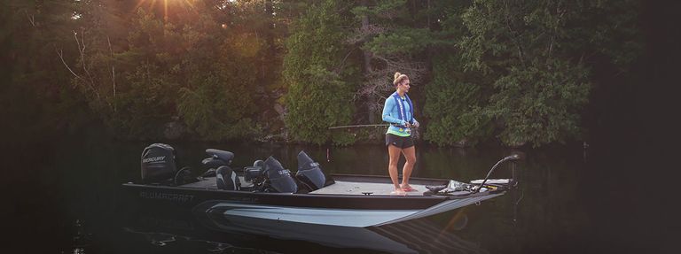 A woman standing at the front of a boat with a fishing pole, boating safety concept.  