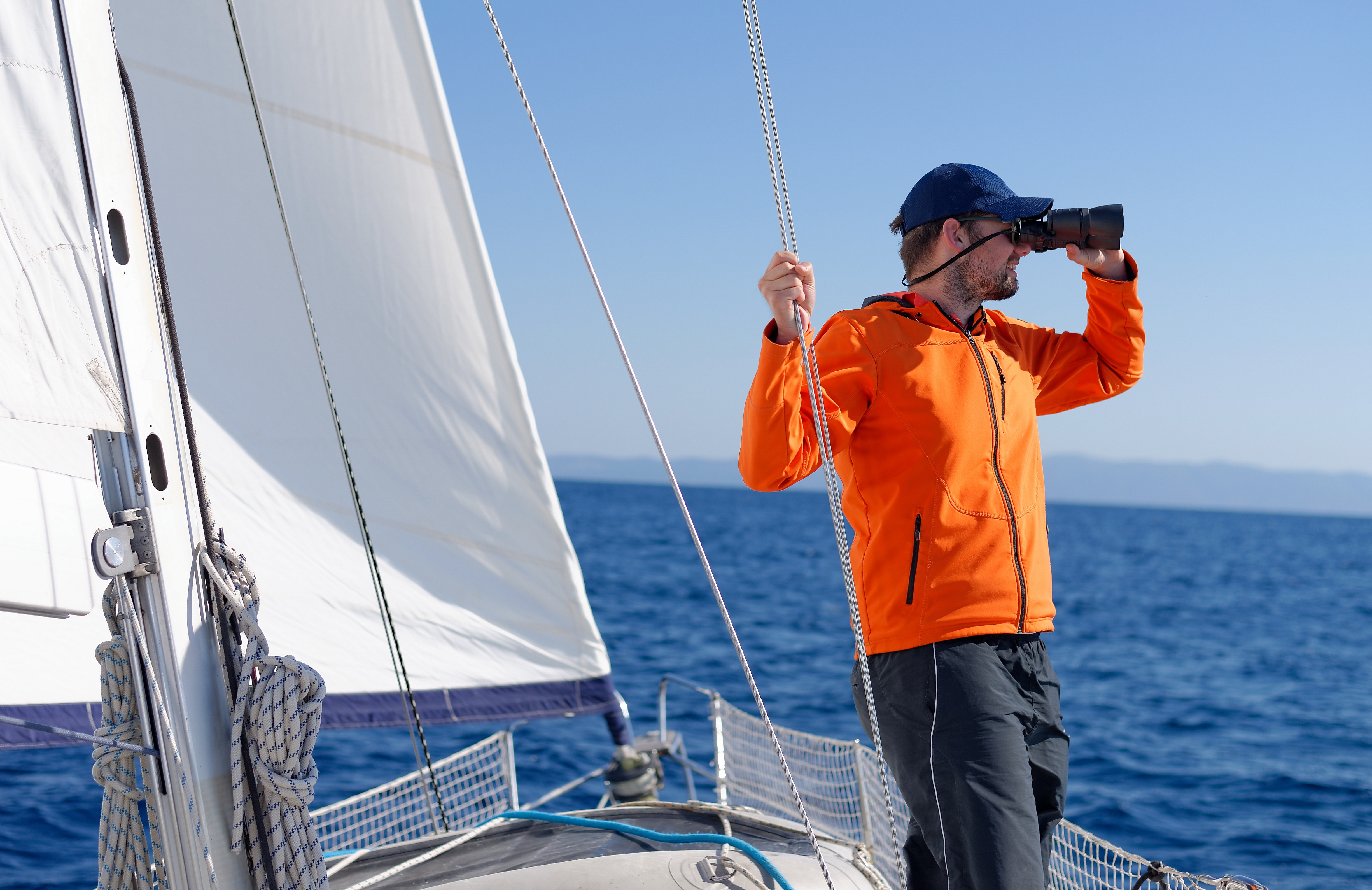 A man using binoculars on a sailboat, answering boat questions concept. 