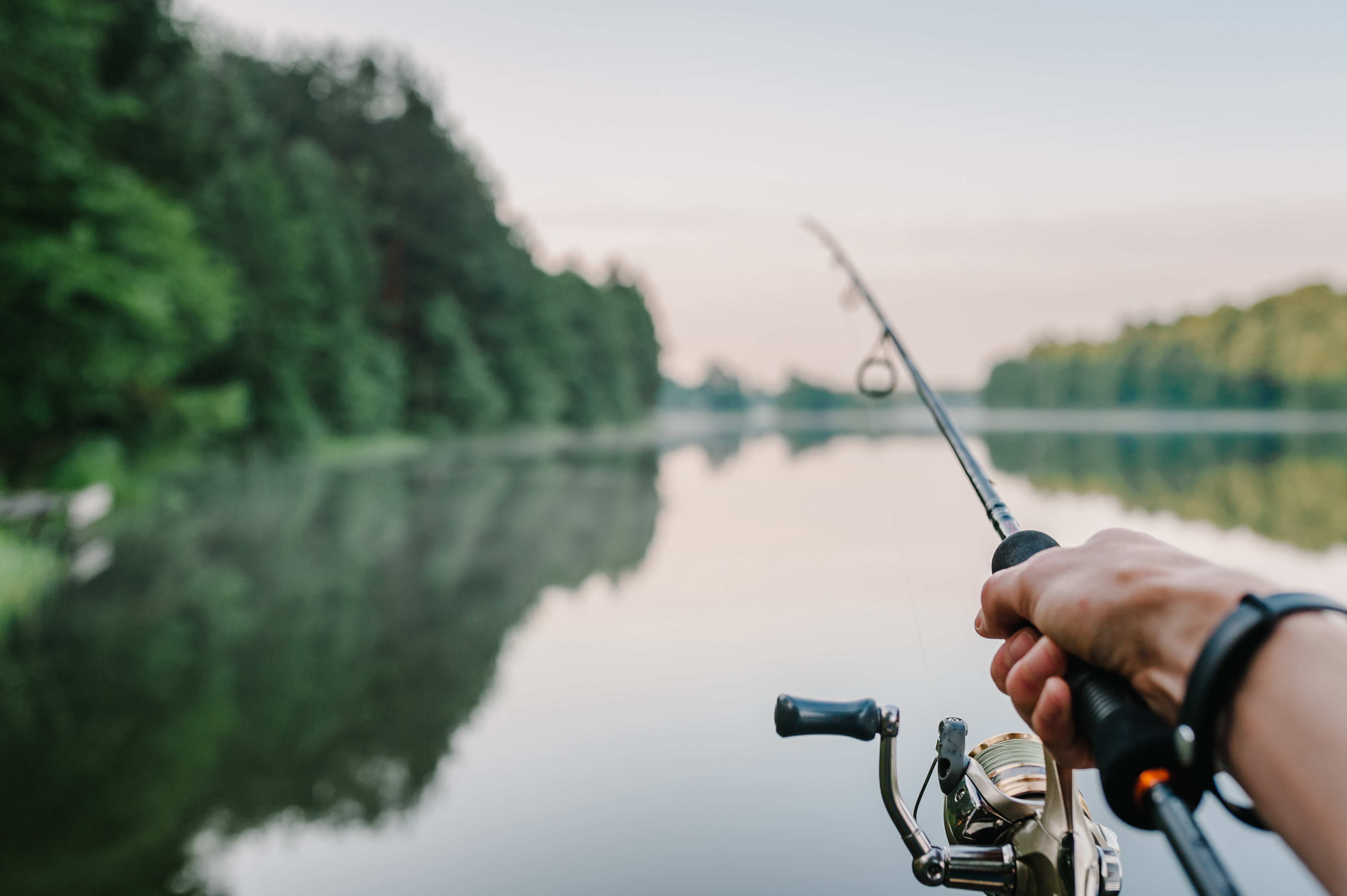 Close-up of a hand holding a fishing rod over the water, bass fishing concept. 