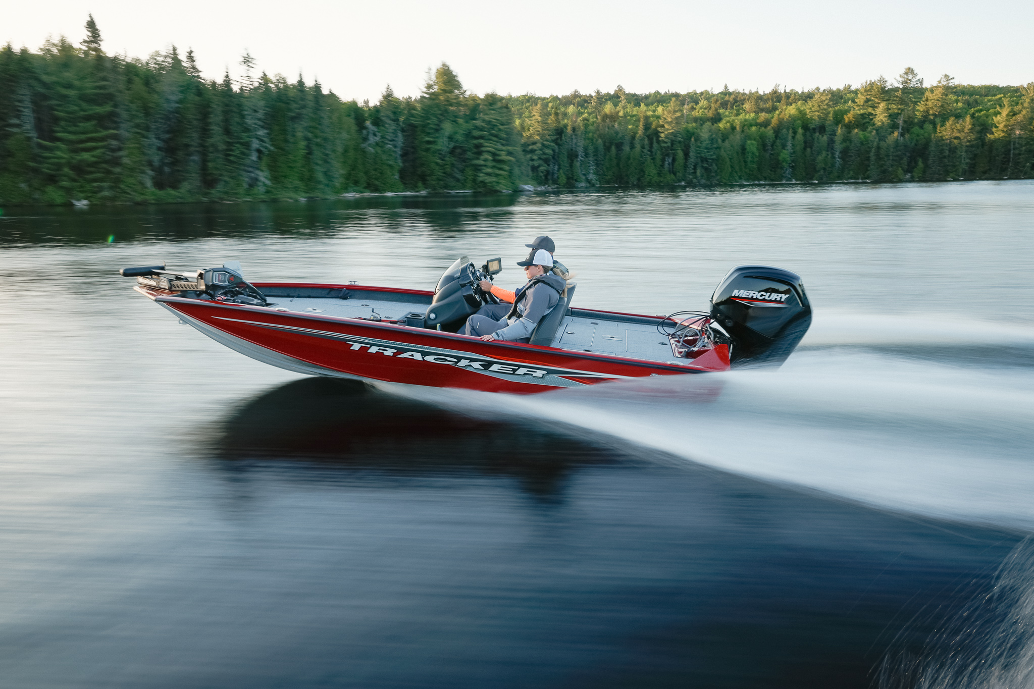 Two people on a fast-moving bass boat on the water.