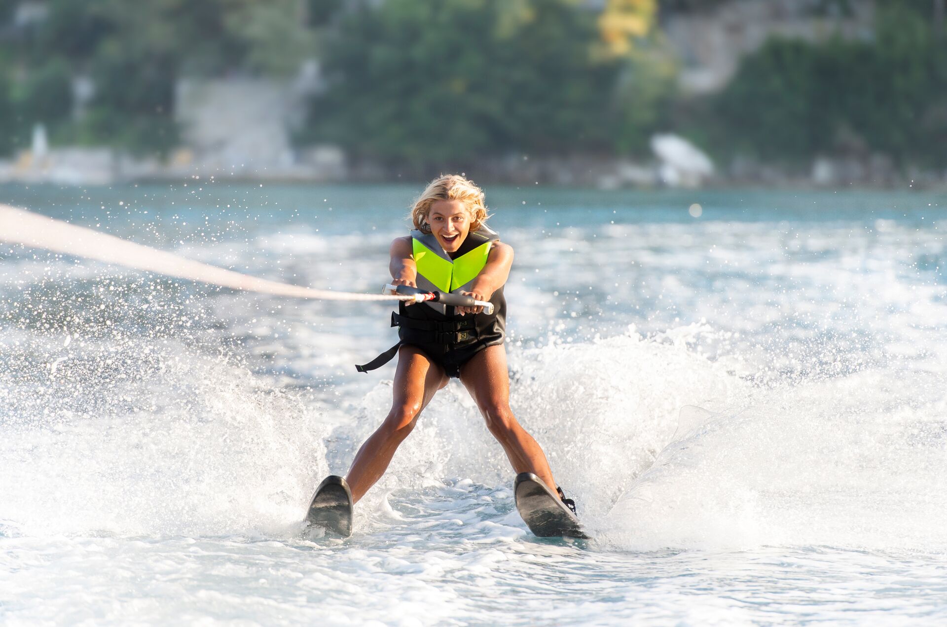 A girl in a yellow life vest on waterskis behind a boat, avoid propeller strikes concept.