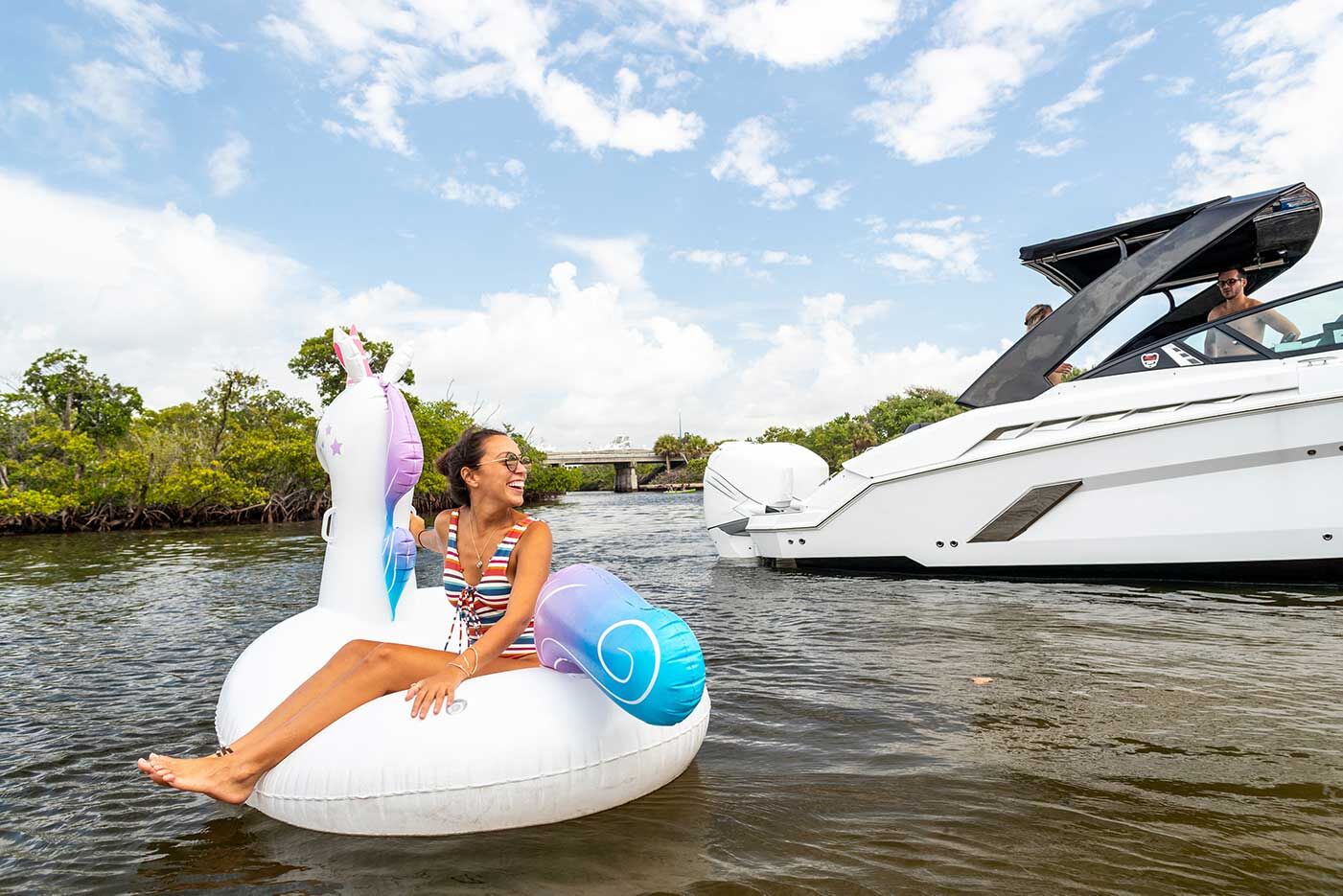 A girl smiling and sitting on a unicorn inflatable near a boat propeller.